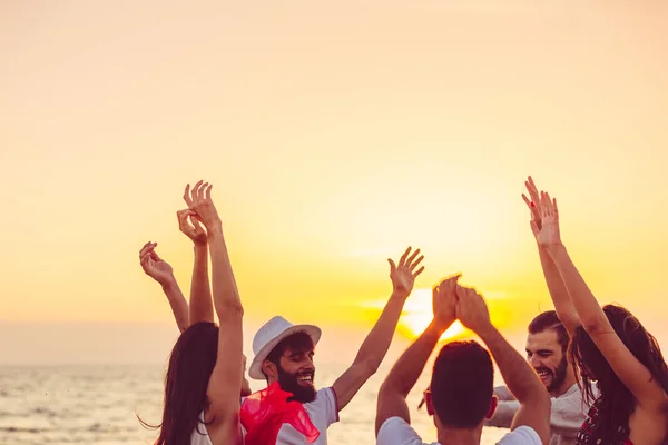 Folk dansar på stranden med händerna upp. — Stockfoto