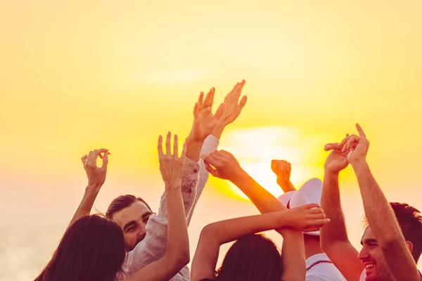 Folk dansar på stranden med händerna upp. — Stockfoto