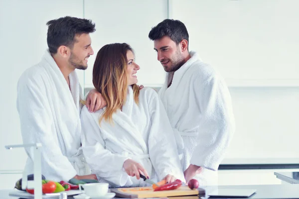 Young people in white bathrobes in kitchen — Stock Photo, Image