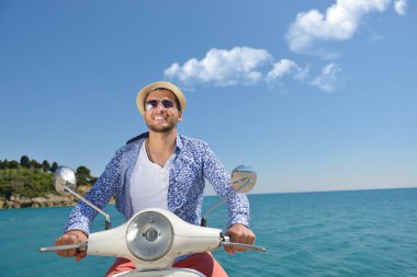 Yakışıklı adam bir tatil bağlamda bir scooter üzerinde poz. Sokak moda ve stil.