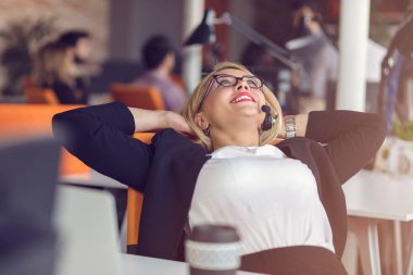 Ellerini başının arkasında tutarak ve ofis onun çalışma evinde otururken gülümseyen güzel genç kadın