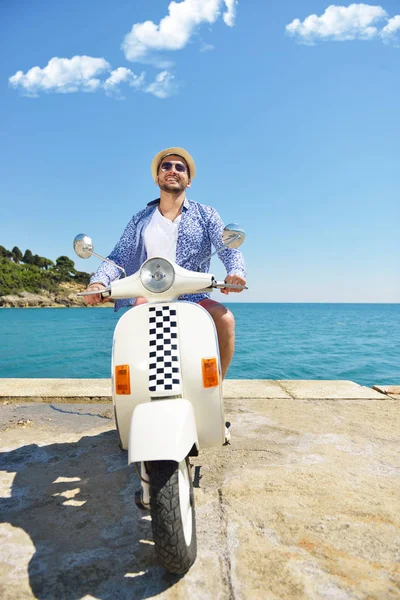 Un hombre guapo posando en una moto en un contexto de vacaciones. Moda y estilo callejero . — Foto de Stock