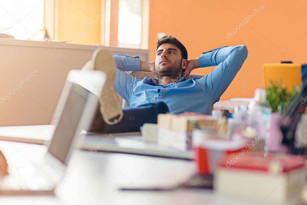 caucasian business person sitting in office thinking daydreaming hands behind head.