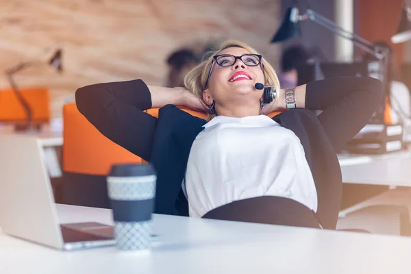 Bella giovane donna che si tiene per mano dietro la testa e sorride mentre si siede al suo posto di lavoro in ufficio — Foto Stock