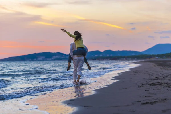 Um cara carregando uma garota de costas, na praia, ao ar livre — Fotografia de Stock