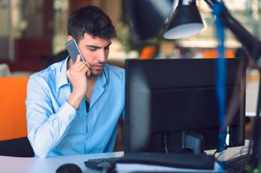 Genç işadamı meşgul ofis akıllı telefonda konuşurken dizüstü bilgisayarda çalışma.