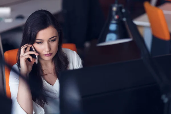 Krásná mladá žena, pracující na počítači a mluví na telefonu — Stock fotografie