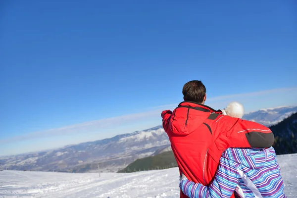 Rear view of a loving couple in fur hood jackets looking at snowed mountain range — Stock Photo, Image