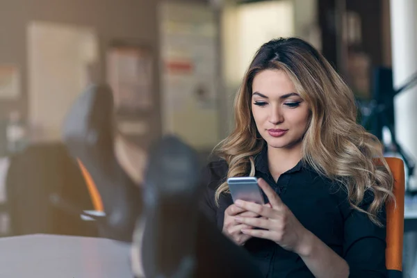 Psaní obchodních zpráv. Jistý mladá žena v chytré oblečení drží chytrý telefon a zíral na ni s úsměvem — Stock fotografie