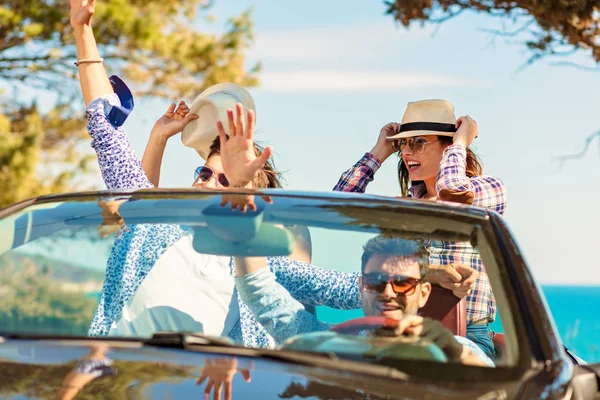 Grupo de jóvenes amigos felices en cabriolet con las manos levantadas conduciendo al atardecer — Foto de Stock