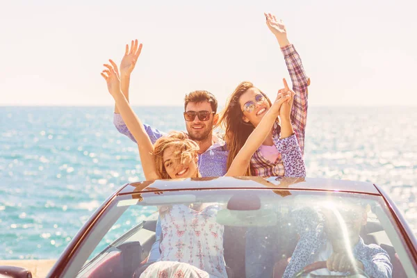 Gruppe fröhlicher junger Freunde im Cabrio mit erhobenen Händen am Sonnenuntergang — Stockfoto