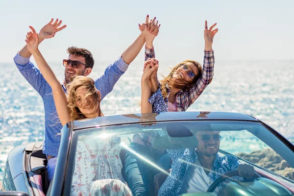 Grupo de jóvenes amigos felices en cabriolet con las manos levantadas conduciendo al atardecer — Foto de Stock