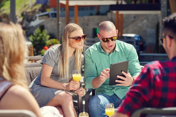 Стильные друзья пользуются цифровым планшетом, пьют кофе и улыбаются, отдыхая в парке — стоковое фото