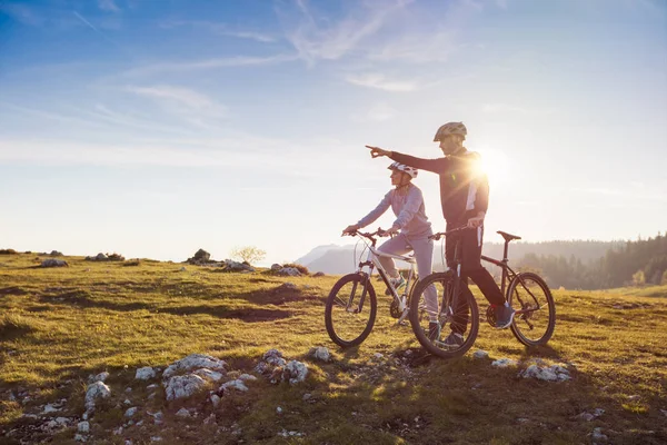 Pareja ciclista con bicicleta de montaña apuntando a la distancia en el campo —  Fotos de Stock