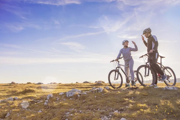 Mutlu çift ormanda bisiklet üzerinde bir dağ asfalt yolda birbirimizi bir beşlik vererek kask ile gider — Stok fotoğraf