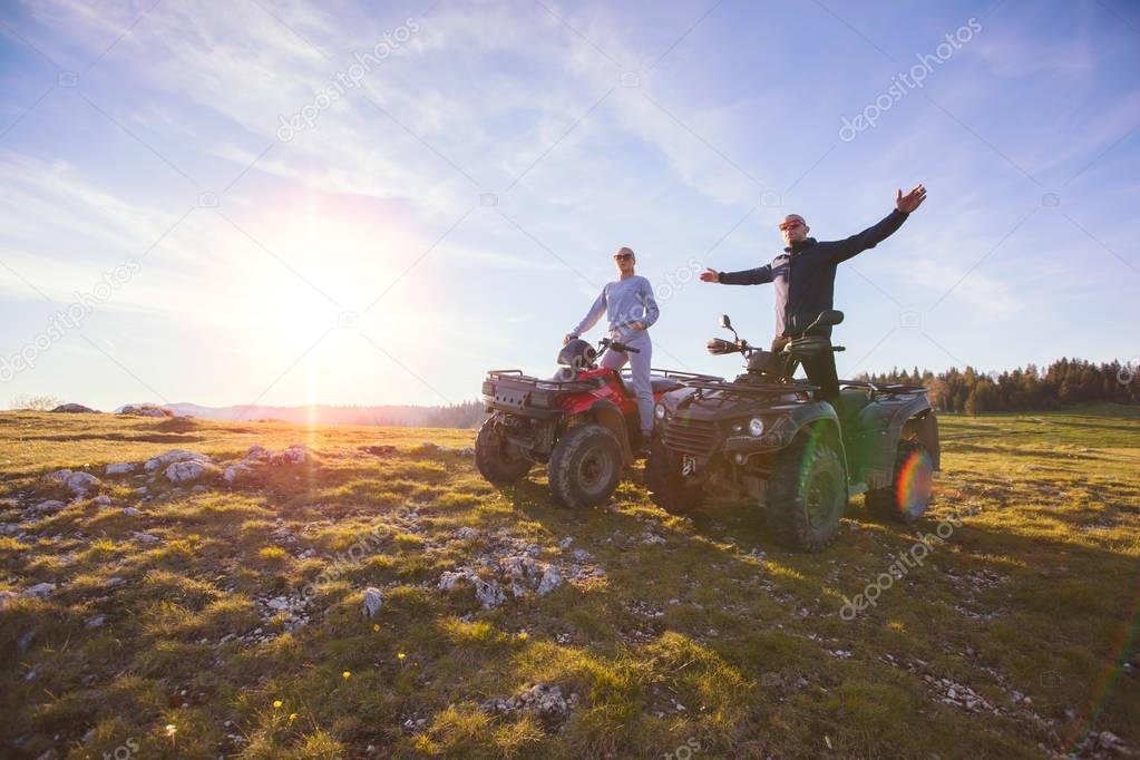 Rear view of young pair near atv. Man is showing something in distance to her girlfriend.