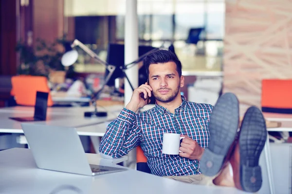 Empresário relaxante com as pernas na mesa, beber café enquanto sonha com o futuro no local de trabalho no escritório moderno . — Fotografia de Stock