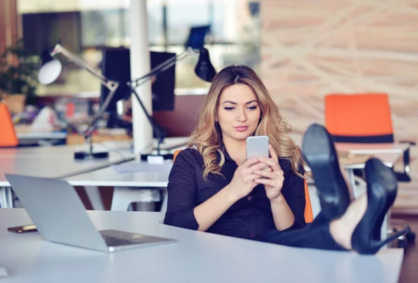 Bella giovane donna sta facendo selfie nel suo posto di lavoro. Si rilassa e mette le gambe sul tavolo . — Foto Stock