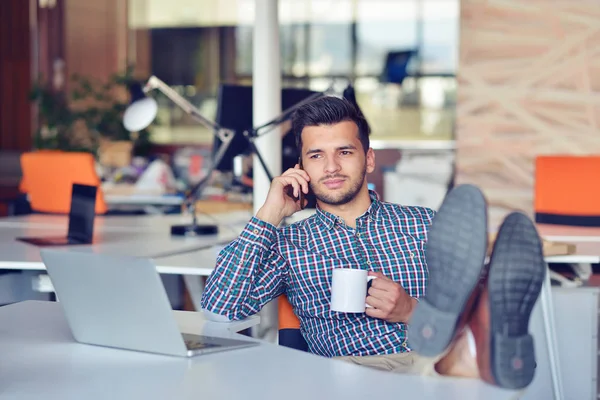 Empresário relaxante com as pernas na mesa, beber café enquanto sonha com o futuro no local de trabalho no escritório moderno . — Fotografia de Stock