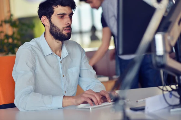 Молодий бізнесмен працює на настільному комп'ютері за своїм столом в сучасному яскравому інтер'єрі стартапу — стокове фото