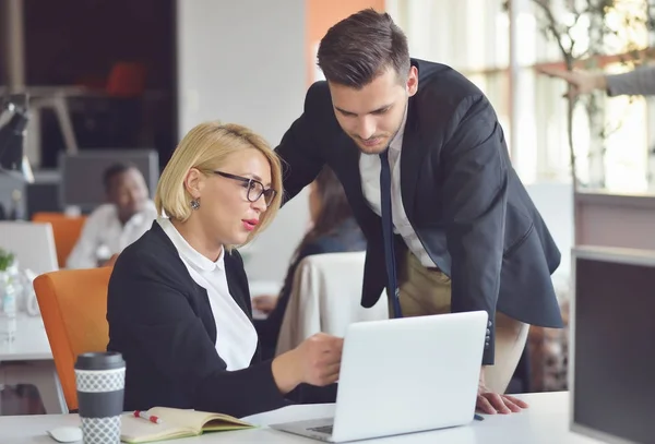 Bei giovani partner commerciali utilizzano un computer portatile, discutono documenti e sorridono mentre lavorano in ufficio. . — Foto Stock