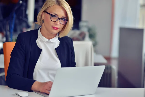 Bella giovane donna che si tiene per mano sul mento e sorride mentre si siede al suo posto di lavoro — Foto Stock