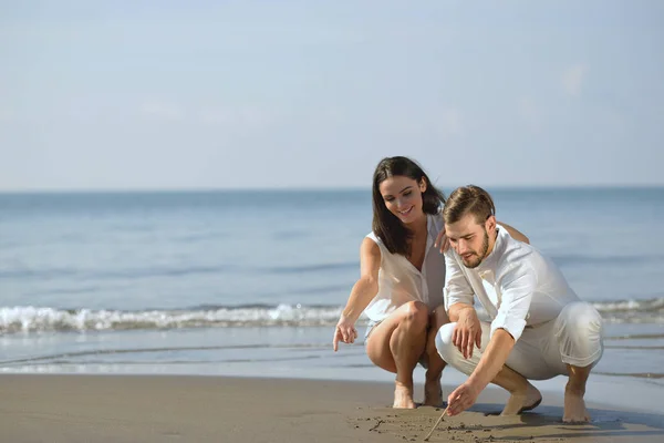 Ein romantisches junges Paar zeichnet während seiner Flitterwochen Herzformen in den Sand. Sommerstrandliebe. — Stockfoto