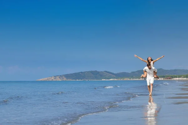 Ein Typ, der ein Mädchen auf dem Rücken trägt, am Strand, im Freien — Stockfoto