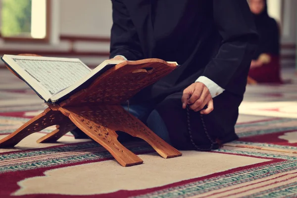 Sebuah quran suci terbuka dengan kayu berdiri dengan orang berdoa di latar belakang — Stok Foto