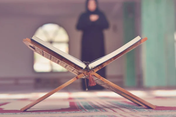 Un sagrado quran abierto con soporte de madera con gente rezando en el fondo — Foto de Stock