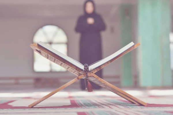 Sebuah quran suci terbuka dengan kayu berdiri dengan orang berdoa di latar belakang — Stok Foto