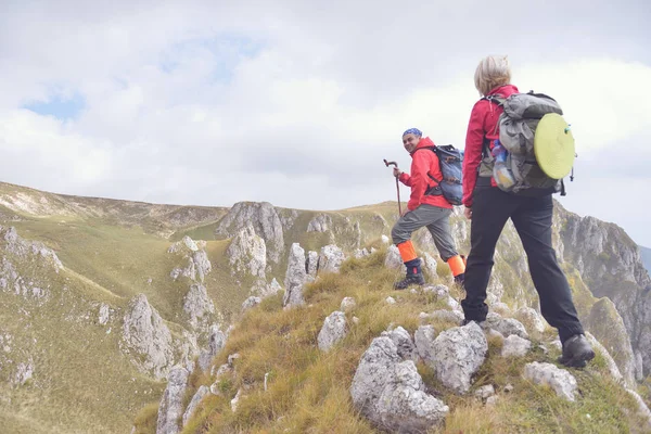 Turyści z plecakami relaksujący się na szczycie góry i cieszący się widokiem na dolinę — Zdjęcie stockowe
