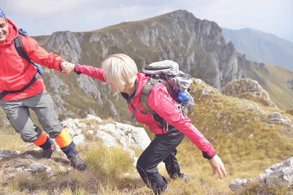 Hombre joven ayudando a mujer escalando montaña — Foto de Stock