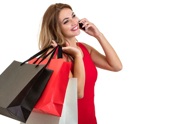 Boldog fiatal nő gazdaság bevásárló táskák és mobiltelefon fehér háttér — Stock Fotó