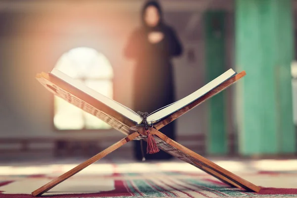 Un Santo Corano aperto con stand in legno con persone che pregano sullo sfondo — Foto Stock