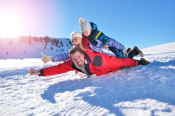Счастливая молодая семья, играющая в свежем снегу в красивый солнечный зимний день на природе — стоковое фото