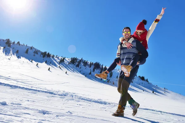 Casal jovem se divertindo na neve. Homem feliz na montanha dando passeio de piggyback para sua namorada sorridente . — Fotografia de Stock