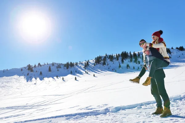 Молода пара розважається на снігу. Щасливий чоловік на горі дає стерво їздити до своєї усміхненої подруги . — стокове фото