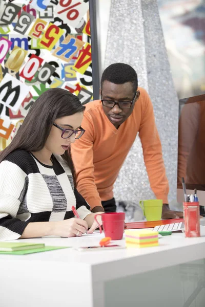 Twee uiteenlopende werken collega's glimlachend en het neerschrijven van notities samen zittend aan een tafel in een modern kantoor — Stockfoto