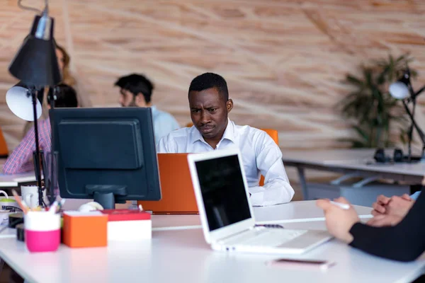 Frustrated young african entrepreneur with sad grimace in front of his laptop in office