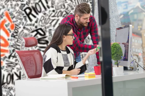 Couple of young designers working at modern office, two coworkers discussing fun project over a laptop,