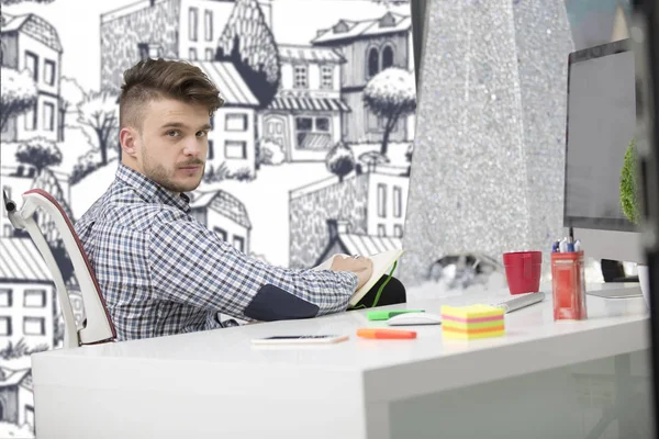 Man taking notes down from his new laptop computer at work in the morning office with coffee