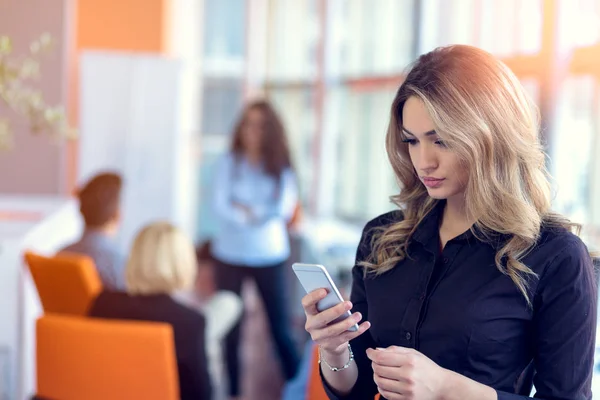 Mladá atraktivní podnikatelka na mobilní telefon v kanceláři, její kolegové na pozadí — Stock fotografie