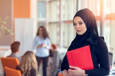 Arabian business woman holding a folder in modern startup office clipart