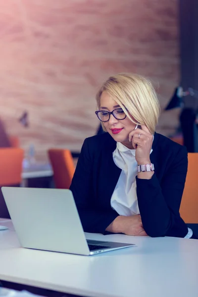 Atrakcyjna kobieta biznes blond czarujący rozmowy na telefon komórkowy siedząc przy biurku pracy na laptopie. — Zdjęcie stockowe