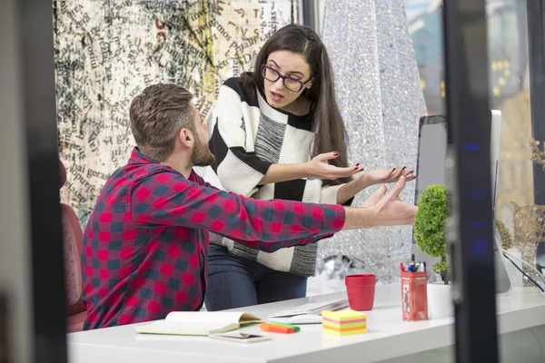 Couple of young designers working at modern office, two coworkers discussing fun project over a laptop,