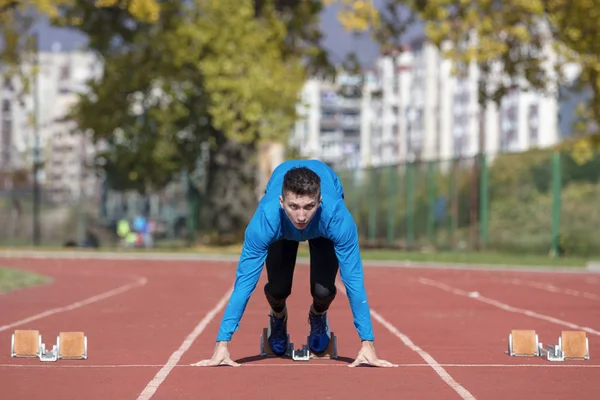 Runner człowieka w niebieską koszulę i szorty i buty sportowe w stabilnej pozycji przed Uruchom na start wyścigu. — Zdjęcie stockowe