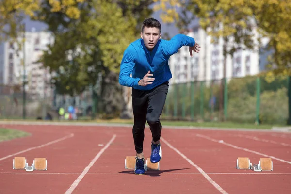Runner człowieka w niebieską koszulę i szorty i buty sportowe w stabilnej pozycji przed Uruchom na start wyścigu. — Zdjęcie stockowe
