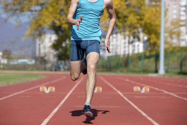 Hombre corredor en camisa azul y pantalones cortos y zapatos deportivos en posición estable antes de correr al inicio de la carrera . — Foto de Stock