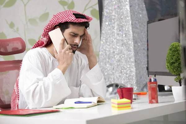 Unga arabiska affärsman som talar på mobiltelefon och fungerande finans om kostnaden med bärbar dator. — Stockfoto